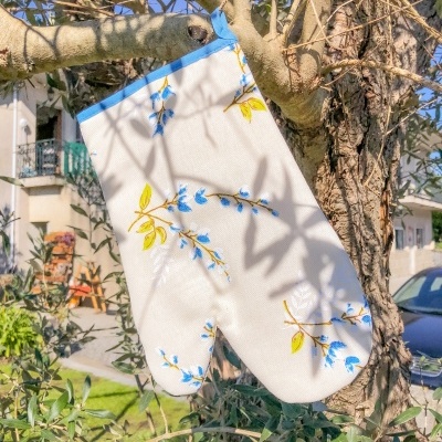 Luva de forno branca com padrão floral azul e amarelo pendurada numa árvore ao ar livre