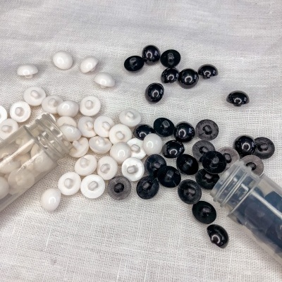 Botões brancos e pretos pequenos em tecido claro com recipientes plásticos