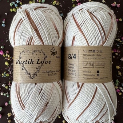 Novelos de fio Rustik Love algodão branco com riscas castanhas em superfície escura com flores coloridas