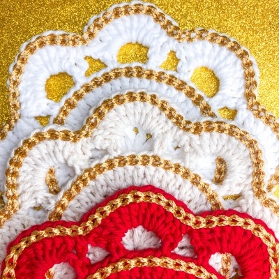 Peças de croché em branco e vermelho com fio dourado em fundo dourado brillante.