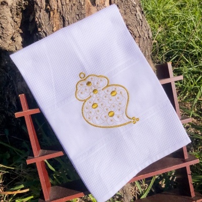 Toalha branca com bordado amarelo sobre estrutura de madeira junto a árvore e relva