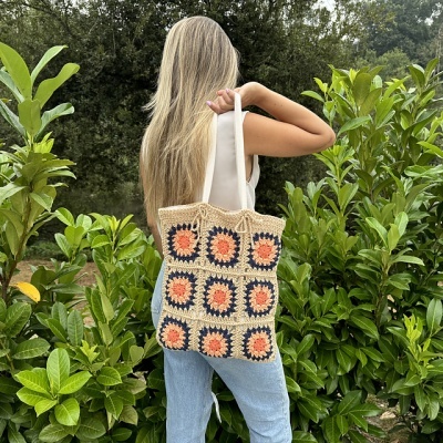 Saco de malha colorido com quadrados sendo usado ao ombro por mulher em exterior