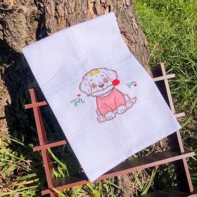 Toalha branca com bordado de cão sorridente e texto 'For You' encostada em árvore