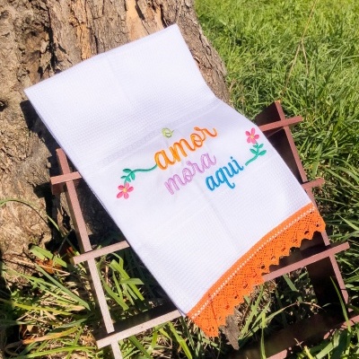 Toalha branca com bordado colorido e barra laranja em estrutura metálica na relva
