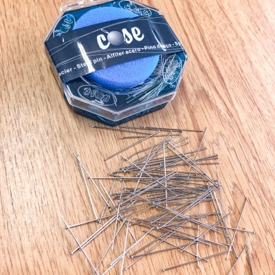 Caixa de agulhas de aço inoxidável com agulhas espalhadas sobre mesa de madeira