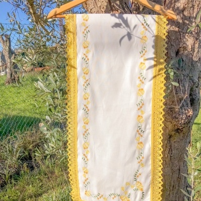 Toalha branca bordada com limões e renda amarela pendurada numa árvore
