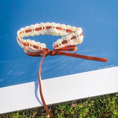 Colar de crochê branco com fita castanha amarrada em laço sobre superfície azul