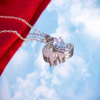 Colar prateado com pendente de coração e pedras brilhantes sobre fundo vermelho e céu azul