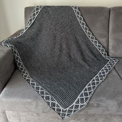 Cobertor preto, cinza e branco com padrão geométrico sobre sofá cinza