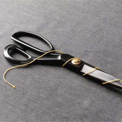 Tesoura grande preta com fio dourado sobre tecido cinzento