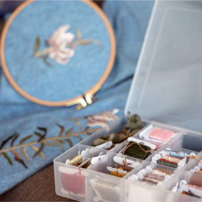 Caixa com linhas para bordado e tecido azul com bordado floral em bastidor.