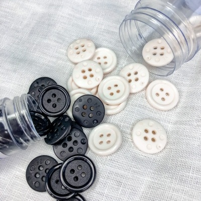 Botões de plástico preto e branco em tecido branco com frascos plásticos.