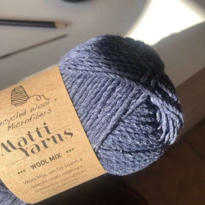 Novelo de lã azul escuro com etiqueta de papel pardo em mesa branca