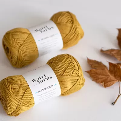 Novelos de fio amarelo mostarda com rótulos e folhas secas ao lado