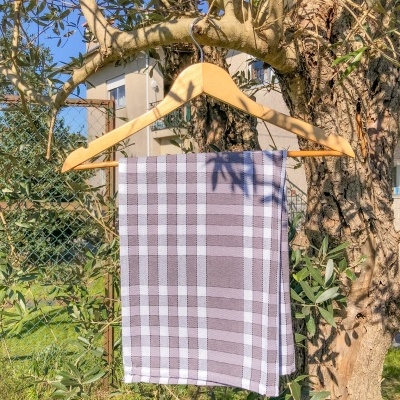 Pano de cozinha xadrez branco e cinza pendurado num cabide de madeira numa árvore ao ar livre