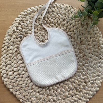 Babete branco creme com acabamento rosa em tapete redondo de corda sobre mesa de madeira clara