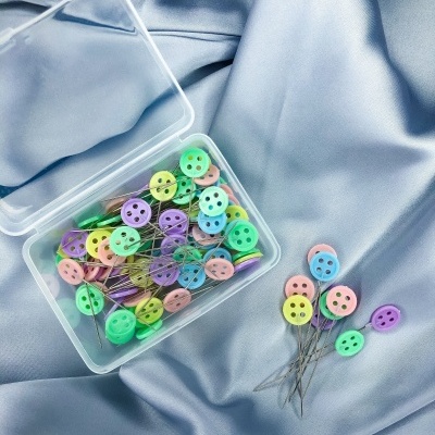 Alfinetes coloridos com cabeça em forma de botão sobre tecido azul acetinado