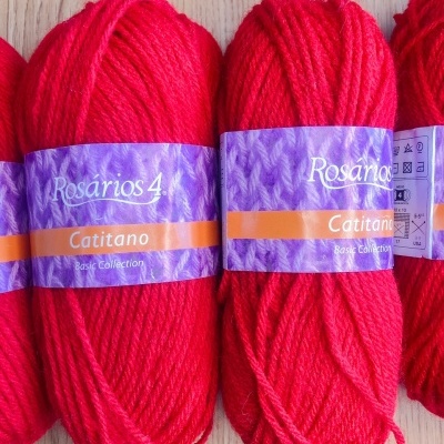 Novelos de lã vermelha Rosários 4 Catitano com etiquetas roxas sobre madeira.