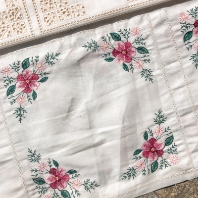 Toalha branca com bordado floral colorido nos cantos.