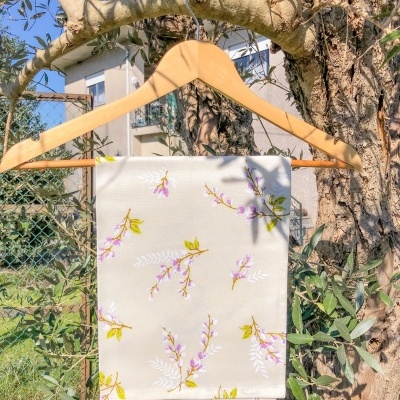 Guardanapo branco com flores rosa e verdes pendurado num cabide de madeira ao ar livre