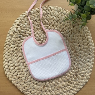 Babete branco com bordas cor-de-rosa em tapete de palha redondo, com planta verde ao lado.
