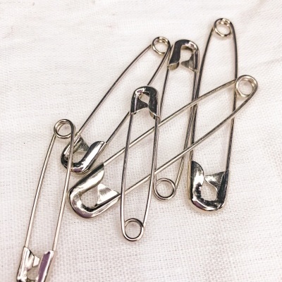 Cinco alfinetes de segurança metálicos prateados sobre tecido branco