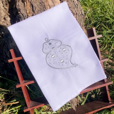 Toalha branca bordada com rato cinza com brilhantes, posto sobre suporte de madeira em ambiente ao ar livre
