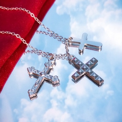 Colares com três cruzes em metal prateado sobre fundo azul e tecido vermelho