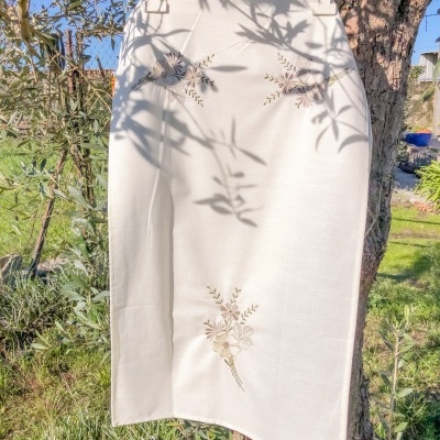 Saia branca com bordados florais pendurada numa árvore ao ar livre