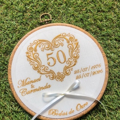 Bastidor bordado redondo branco com texto em dourado e fita branca sobre relva