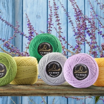 Novelos de linha coloridos sobre madeira com flores roxas ao fundo