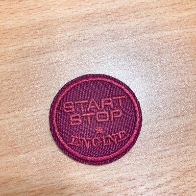 Emblema redondo bordô com texto START STOP ENGINE em tecido sobre madeira clara