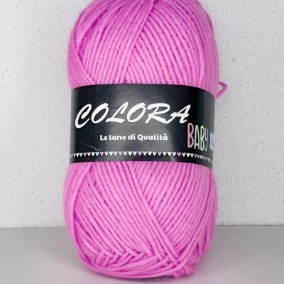 Novelo de lã cor rosa com etiqueta preta e texto branco e colorido, sobre superfície cinza claro com fundo branco