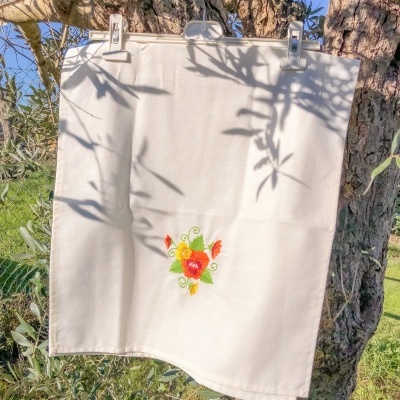Pano de cozinha branco com bordado de flores pendurado numa árvore ao ar livre