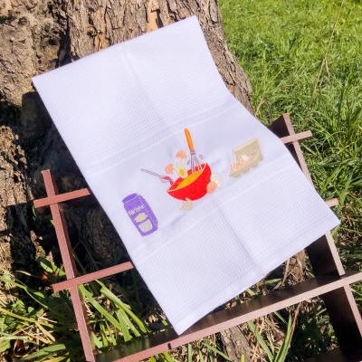 Toalha branca com ilustrações de cozinha apoiada em suporte de madeira junto a árvore