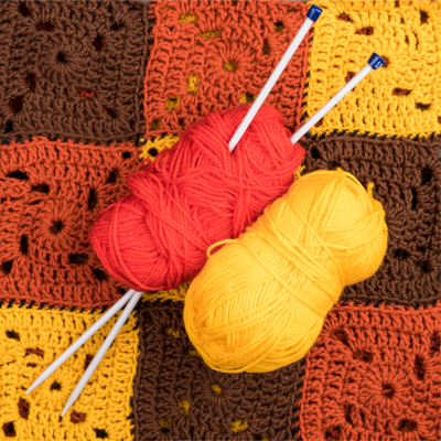 Dois novelos de lã com agulhas de tricô sobre manta de croché colorida