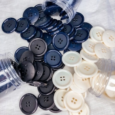 Três frascos transparentes com botões pretos, azuis e brancos sobre tecido branco