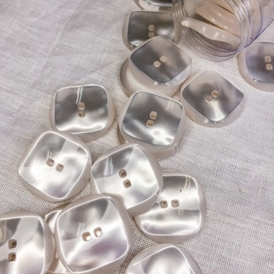 Botões quadrados perolados brancos sobre tecido branco com frasco plástico