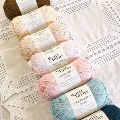 Seis novelos de lã coloridos da marca Matti Yarns sobre tecido com renda branca.