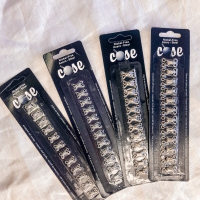 Quatro conjuntos de ganchos e olhos em aço prateado embalados em cartão preto