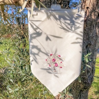 Pano branco com desenho de vaso de flores pendurado numa árvore de oliveira
