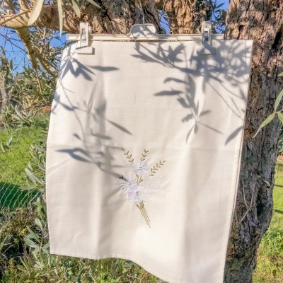 Pano branco com bordado floral pendurado numa árvore ao ar livre