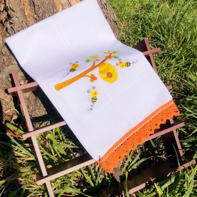 Toalha branca bordada com tema de abelhas e colmeia com barra de crochê laranja.