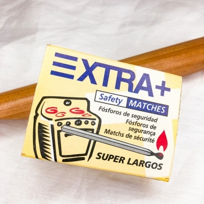 Caixa amarela de fósforos Extra+ com fósforo aceso e texto em várias línguas