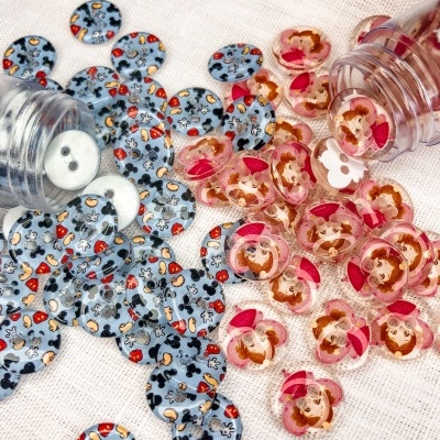 Dois frascos transparentes com botões decorativos azuis e rosa sobre tecido claro