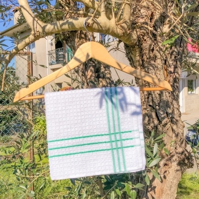 Toalha branca com linhas verdes pendurada num cabide de madeira numa árvore ao ar livre