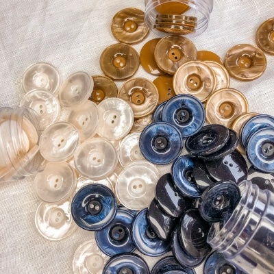 Botões redondos de plástico em castanho, azul marmoreado e bege sobre tecido branco