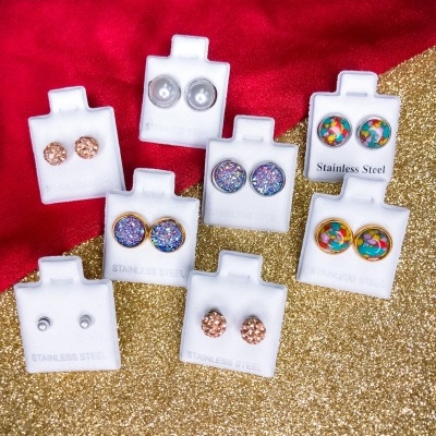 Brincos coloridos em aço inoxidável em suportes de cartão branco sobre fundo vermelho e dourado