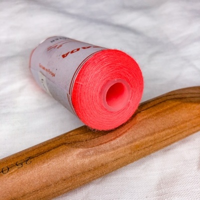 Rolo de linha vermelho vivo com carretel plástico e objeto de madeira polida sobre tecido branco