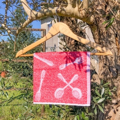 Toalha vermelha com padrão de colheres branca pendurada em cabide de madeira numa árvore